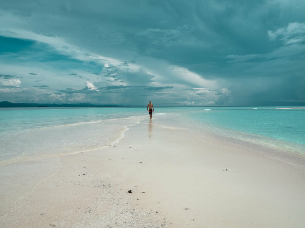 homme qui marche sur un banc de sable au milieu de la mer à Raja Ampat